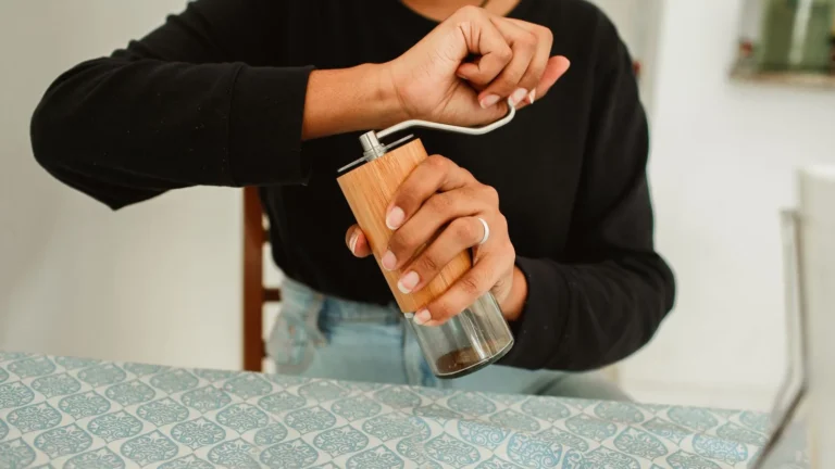 A person turning the handle of a manual burr coffee grinder