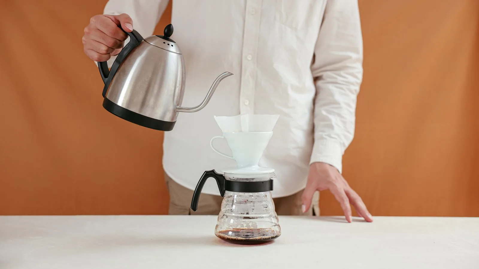Gooseneck kettle pouring water through a cone dripper into a glass carafe