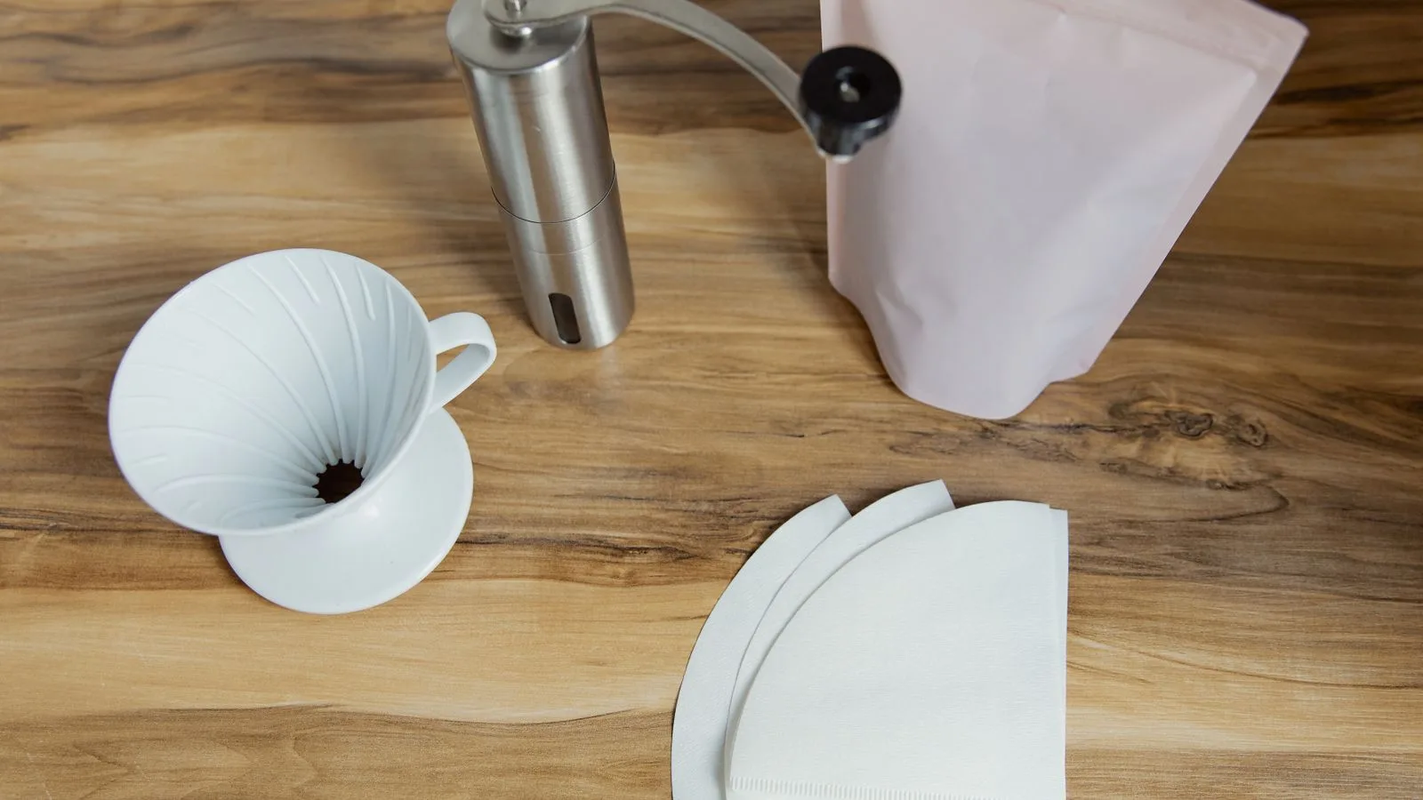 Pour over dripper, hand grinder, paper filters and a bag of coffee on a wooden table