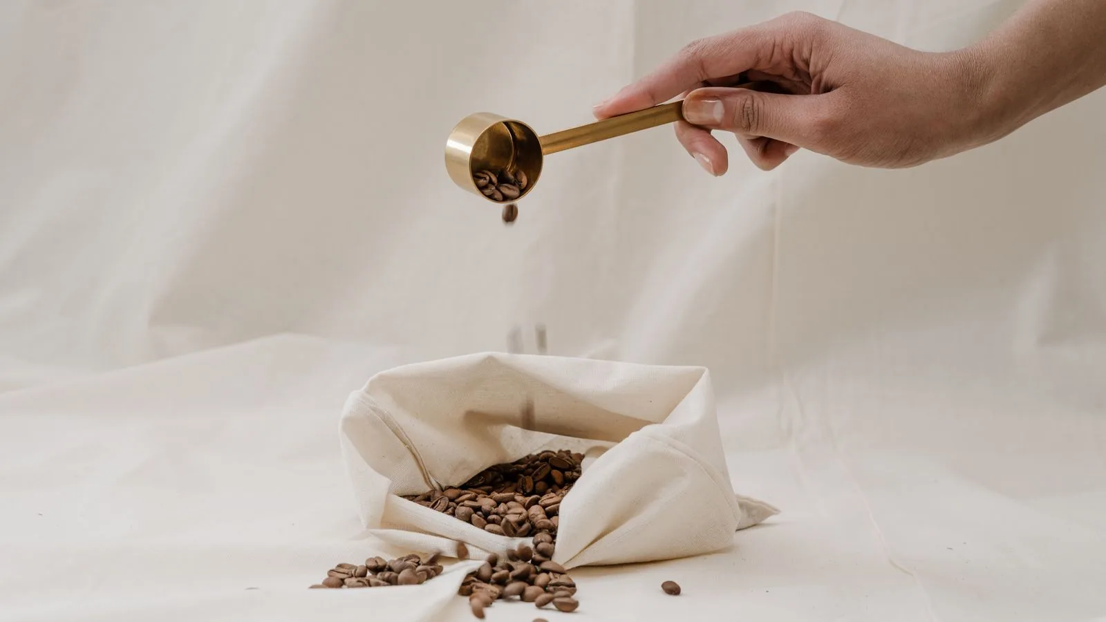 Coffee beans poured from a scoop into a cloth bag