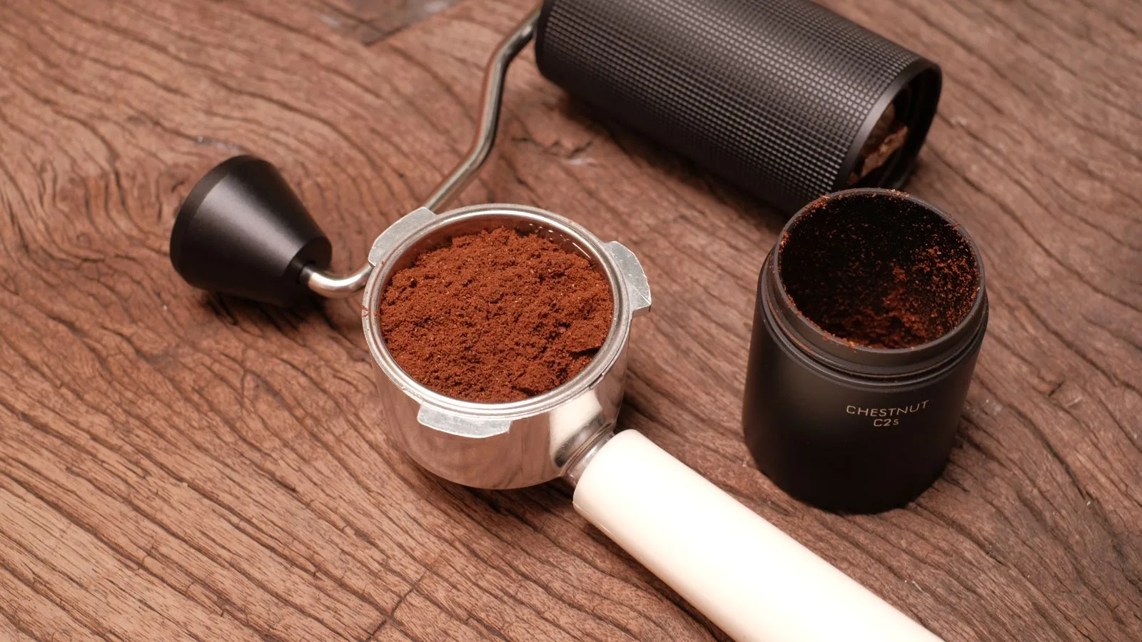 Hand coffee grinder beside a portafilter filled with fresh grounds