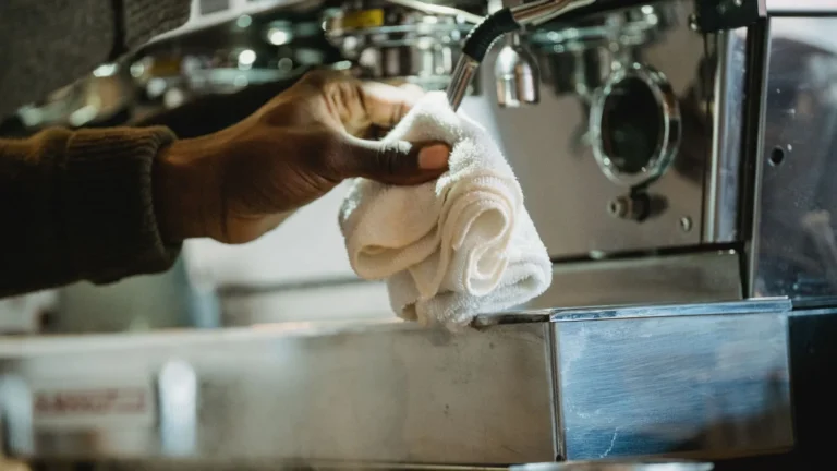 Someone wiping down an espresso machine with a cloth