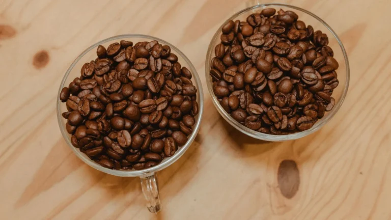 Two glass cups of roasted coffee beans side by side on a wooden surface